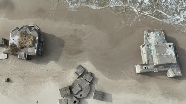 Overhead drone footage of two abandoned military bunkers on a Danish beach with waves moving across the shoreline. Ideal for military history, coastal erosion, aerial landscapes and documentary themes