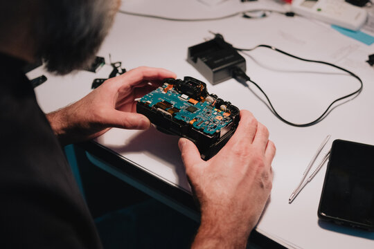 Electronics technician repairing a disassembled digital camera circuit board at a technical service workbench