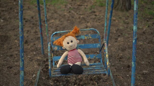 Old Plush Girl Doll Swaying on Peeling Swings in a Dark Park
