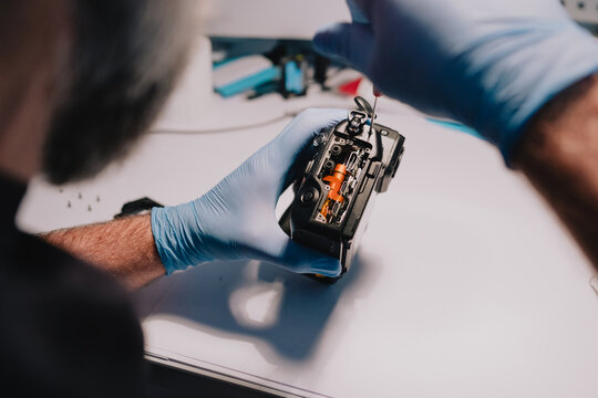 Camera repair technician wearing protective gloves servicing exposed internal components of a digital camera at a technical workbench