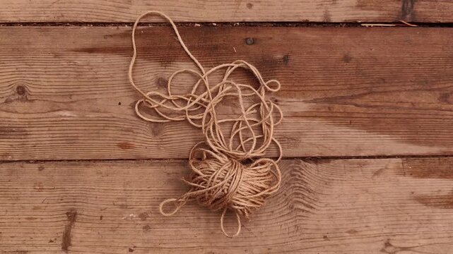 Coil of natural jute rope lands on rustic wooden boards with visible texture, packaging material, handmade craft, eco supplies, natural fiber.