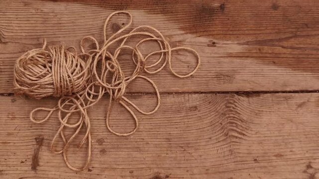 Coil of natural jute rope resting on rustic wooden boards with visible grain and wet texture, eco packaging material, handmade craft, natural fiber.