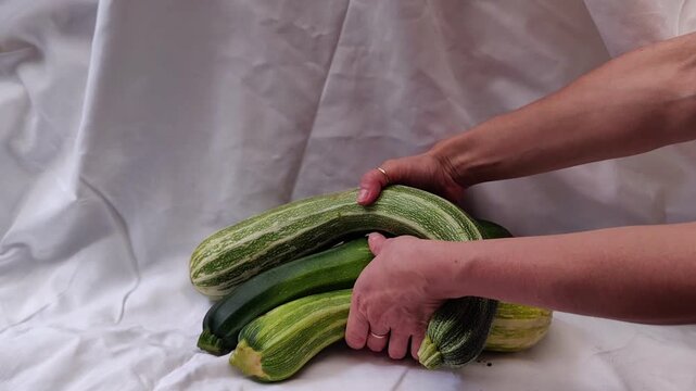 Woman removes three fresh zucchini from a white tablecloth, organic vegetables, healthy lifestyle, farm produce, minimalist food styling.