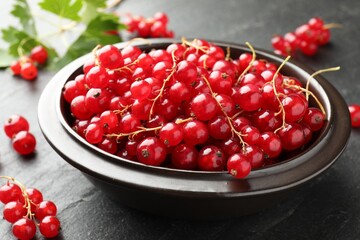 Fresh red currants in bowl and green leaves on dark grey textured table, closeup © New Africa