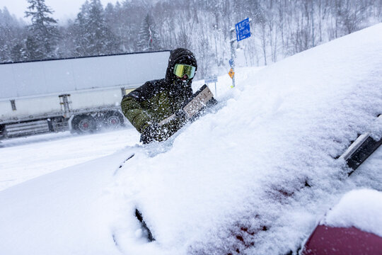 Skier shoveling heavy snow off car during winter storm