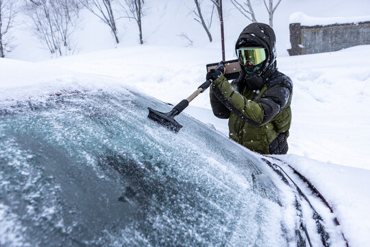 Skier scraping ice from car windshield during blizzard