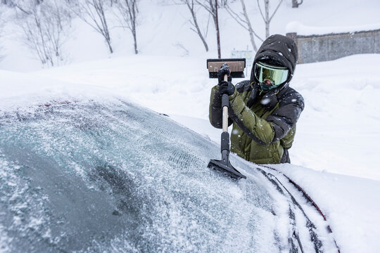 Skier scraping ice from car windshield during blizzard