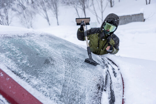 Skier scraping ice from car windshield during blizzard