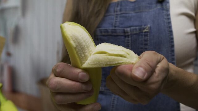 Closeup, slow motion shot of woman peeling banana and slicing it up with knife on cutting board