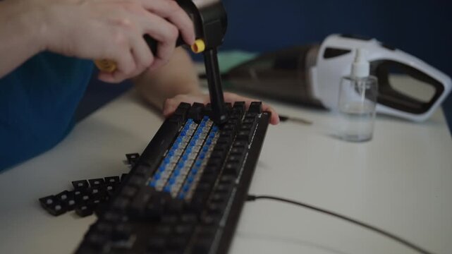 Detailed process of technician using portable electric air blower to clean switches of dirty mechanical keyboard after removing keycaps for deep maintenance. Shooting in slow motion