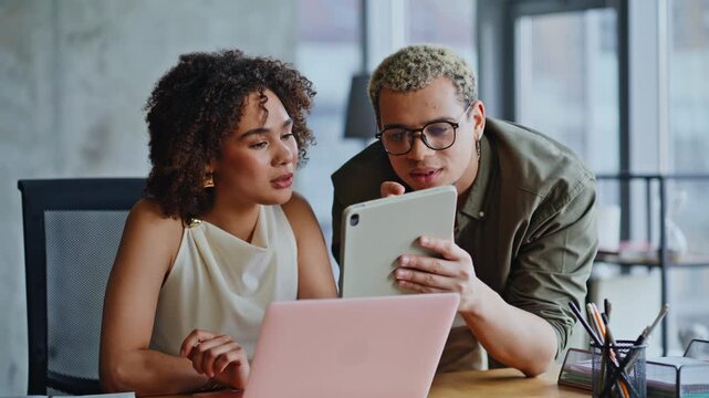 Colleagues reacting to shocking news on tablet in office, worried woman at desk