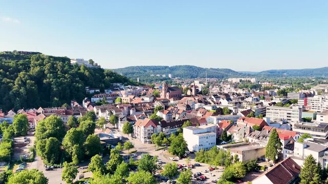 Malerische Ansicht von Homburg an der Saar mit der markanten Stadtkirche, dichten gr&uuml;nen B&auml;umen im Vordergrund und dem bewaldeten Schlossberg unter blauem Sommerhimmel.
