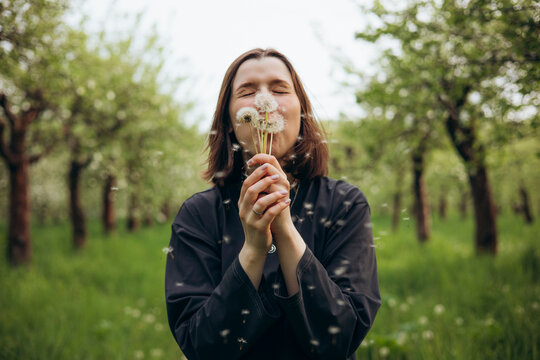 Woman blowing dandelion seed in spring orchard meadow