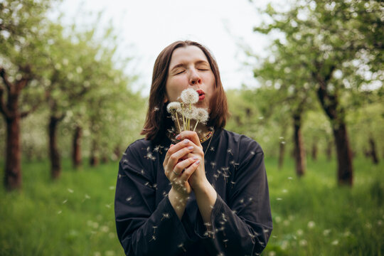 Woman blowing dandelion seeds in spring orchard nature