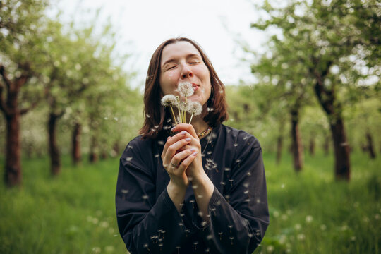 Woman blowing dandelion seed in spring orchard nature