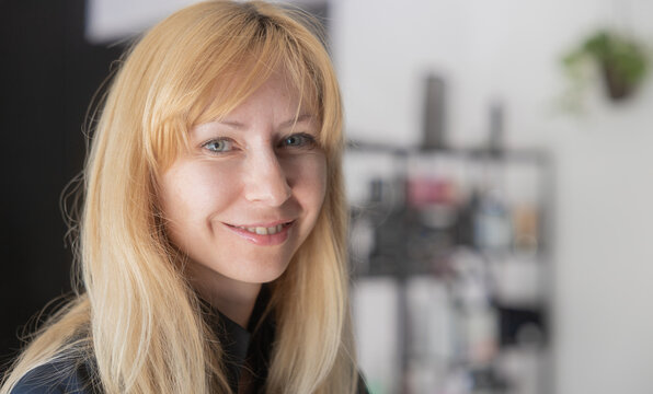 Smiling blonde hairstylist portrait in modern salon interior