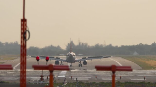 Commercial passenger plane decelerating on runway after landing with spoilers deployed during warm sunset with heavy heat haze, telephoto rear view