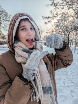 Smiling girl tasting icicle in frosty winter park