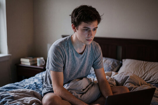 Gay Creator Vulnerability: Young man sits pensive after broadcast on rumpled bed.