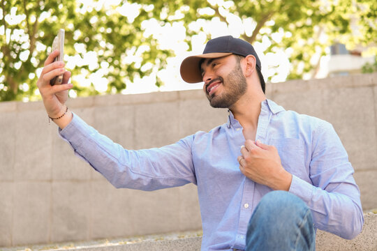Man taking smartphone selfie outdoors in casual cap