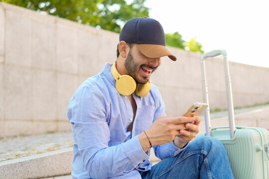 Smiling traveler using smartphone with luggage outdoors