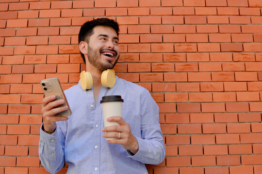Smiling man with smartphone and coffee by brick wall