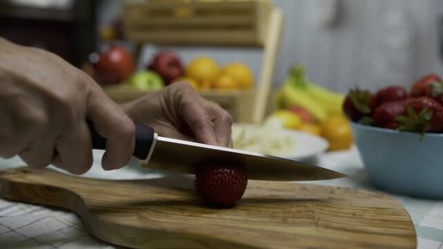 Slow motion closeup shot of knife cutting up strawberry on wooden board