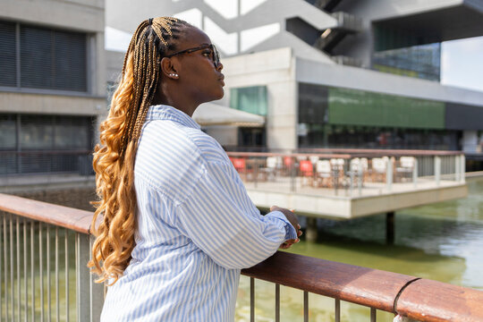 Black woman with long braids leaning on city railing