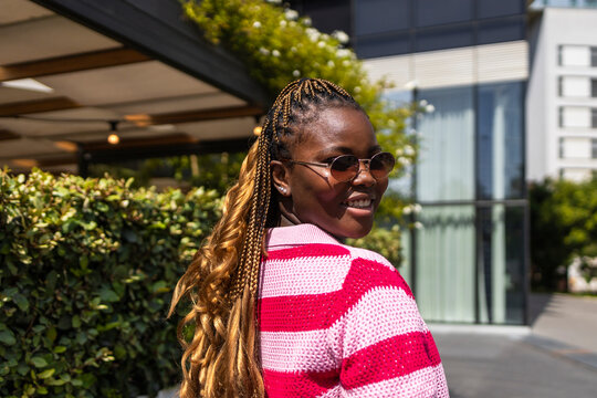 Smiling Black woman with braids in city street sunlight