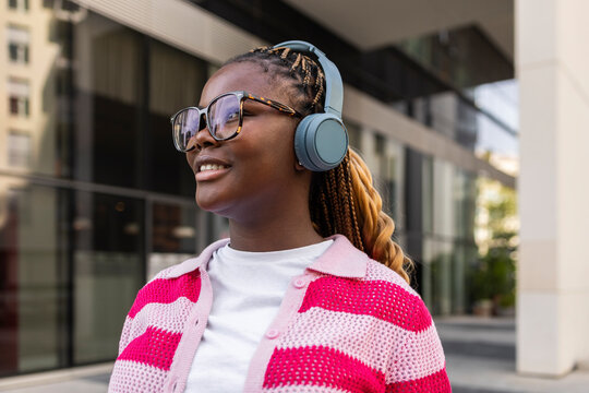 Smiling Black woman with braids wearing headphones outdoors