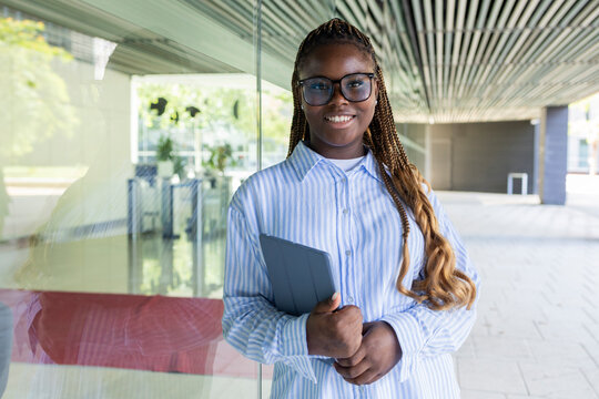 Smiling Black woman with braids holding laptop outdoors