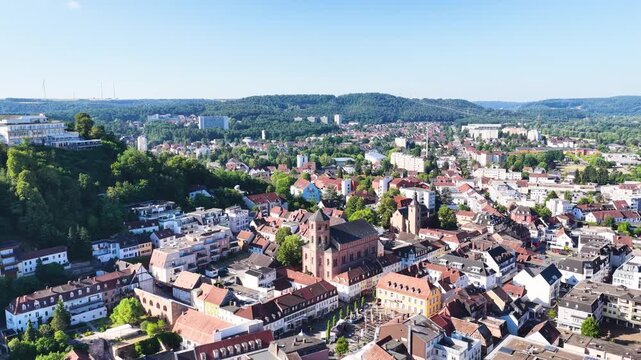 Malerische Ansicht von Homburg an der Saar mit der markanten Stadtkirche, dichten gr&uuml;nen B&auml;umen im Vordergrund und dem bewaldeten Schlossberg unter blauem Sommerhimmel.