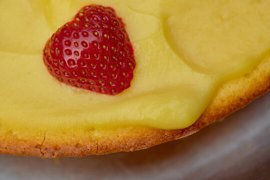 Extreme close up of a juicy red strawberry half on yellow pastry cream and baked tart crust