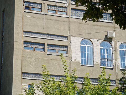 Close-up of the architectural transition between an old industrial facade with glass blocks and a newly renovated section with modern arched windows.