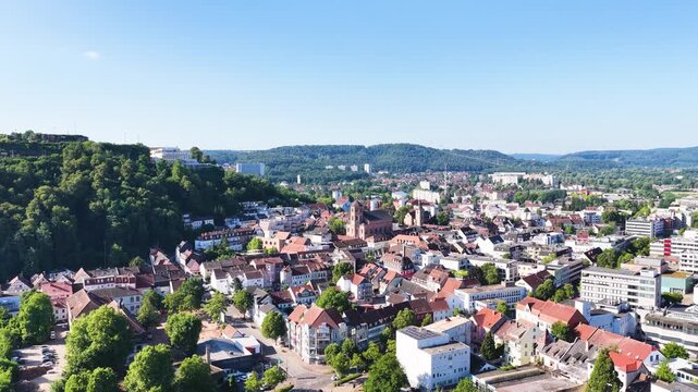 Malerische Ansicht von Homburg an der Saar mit der markanten Stadtkirche, dichten gr&uuml;nen B&auml;umen im Vordergrund und dem bewaldeten Schlossberg unter blauem Sommerhimmel.