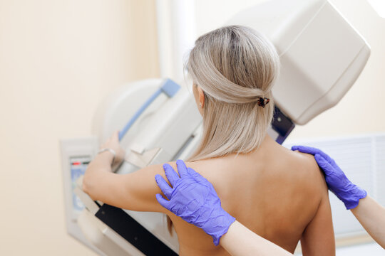 Woman positioned for breast imaging in radiology room with mammogram machine