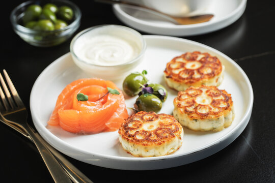 Savory Syrniki with Smoked Salmon, Olives and Sour Cream on White Plate