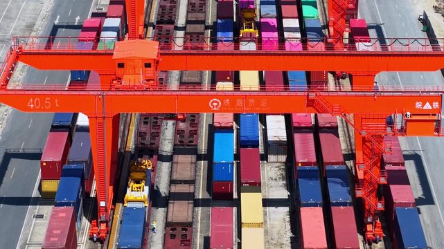 Aerial top-down view of container port with red quay cranes, cargo ships and colorful shipping containers
