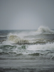 Naklejka premium Powerful ocean waves breaking under an overcast sky with sea spray and rough water. Ideal for seascapes, coastal weather, marine environments and nature themes.