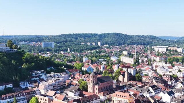 Malerische Ansicht von Homburg an der Saar mit der markanten Stadtkirche, dichten gr&uuml;nen B&auml;umen im Vordergrund und dem bewaldeten Schlossberg unter blauem Sommerhimmel.