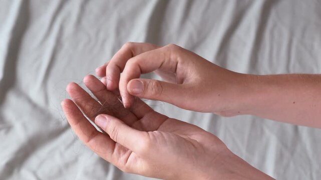 Woman holds clump of fallen hair in hands after brushing. Close up showing excessive hair shedding at home. Hair loss, alopecia awareness, scalp health, beauty care and wellness concept.