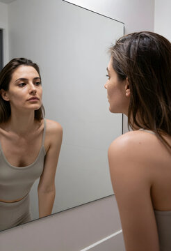 Young woman looking at her reflection in a bathroom mirror, self care and skin health concept, natural beauty and wellness