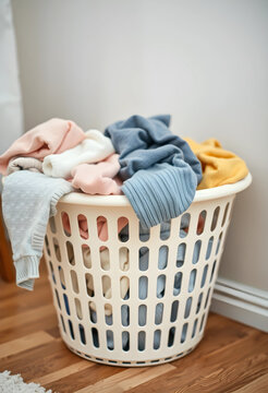 White laundry basket overflowing with colorful dirty clothes on a wooden floor household chores and domestic life
