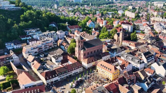 Malerische Ansicht von Homburg an der Saar mit der markanten Stadtkirche, dichten gr&uuml;nen B&auml;umen im Vordergrund und dem bewaldeten Schlossberg unter blauem Sommerhimmel.