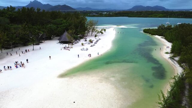 Aerial view capturing the iconic coastal layout of Ile aux Cerfs (Deer Island), Mauritius. Winding turquoise lagoon channel with clear shallow water, bordered by an expansive white sand beach featurin