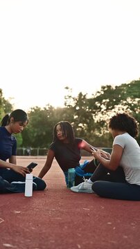 Group of diverse athletic women sitting on a running track taking a selfie with a smartphone