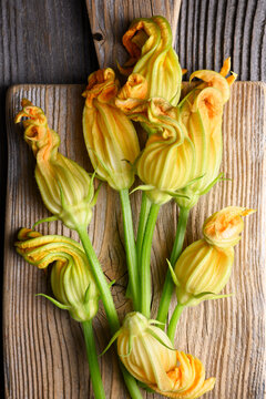 Top view zucchini blossoms on wooden board close composition. Fresh edible flowers with vibrant yellow tones and natural texture
