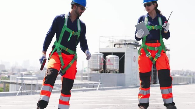 Two solar technicians working on rooftop photovoltaic installation, one drilling panel mounts while colleague checks system data on a tablet.