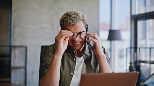 Anxious freelancer talking phone rubbing eyes at laptop desk. Bad news call.