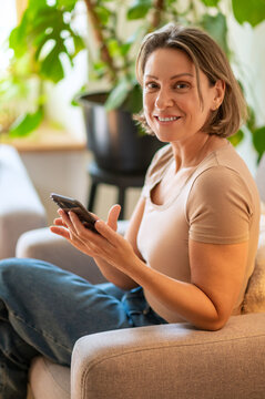 Happy middle aged woman looking at camera with smartphone